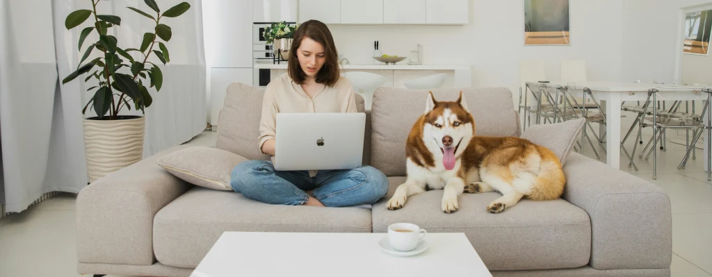 Mujer joven mirando un ordenador al lado de su perro y haciendo cursos online